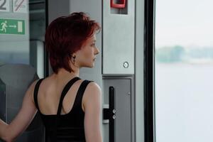 girl stands in a carriage of a moving suburban train in front of the door, looking at the sea photo