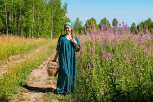 young woman in folk peasant clothes with a wicker basket walks along a field road photo