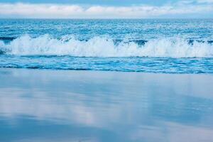 seascape, ocean surf on a smooth sandy beach, the sky is reflected in the wet sand photo