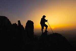 silueta de un trepador a el parte superior de el rocoso montaña a atardecer, hombre en parte superior de montaña. conceptual diseño. solo a el cumbre trepador exitoso escaladores deporte y activo vida. foto