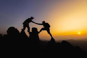 siluetas de dos personas alpinismo en montaña y Ayudar. trabajo en equipo de dos hombres caminante Ayudar cada otro en parte superior de montaña alpinismo equipo hermosa amanecer. ayuda y asistencia concepto. foto