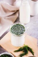 Glass with fresh Turkish ayran with dill and greens on the table vertical view photo