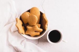 Close up of bowl with sweet mug-hugging cookies and cup of coffee top view photo