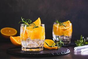 Carbonated cocktail with orange, ice and rosemary in glasses on the table photo