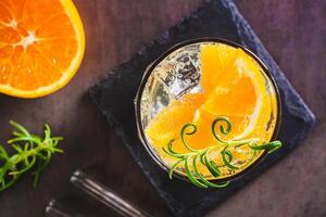 Close up of carbonated cocktail with orange, ice and rosemary in a glass on the table top view photo