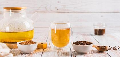 Fresh buckwheat tea in a glass, teapot and granules in a bowl on the table  web banner photo