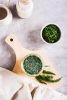 Glass with fresh Turkish ayran with dill and greens on the table top and vertical view photo