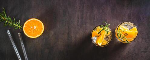 Hard seltzer with ice, orange and rosemary in glasses on the table top view web banner photo