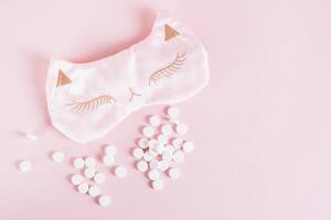 Sleeping pills and sleep mask on pink background top view photo