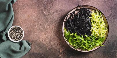 Noodles with cuttlefish ink, cucumber and arugula on a plate on the table top view web banner photo