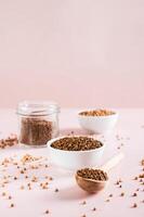 Dry buckwheat tea granules in a bowl, spoon and jar on the table vertical view photo