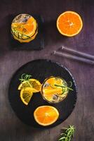 Hard seltzer with ice, orange and rosemary in glasses on the table top and vertical view photo