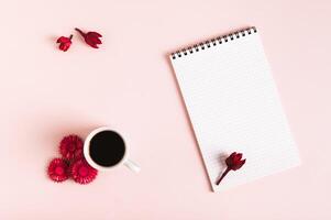 Cup of coffee, dried flowers and open notebook on pink background top view photo