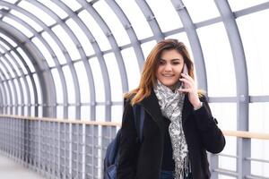 young woman is walking along the covered pedestrian overpass, talking on the phone photo