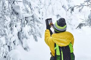 woman traveler in winter forest records video with herself by smartphone photo