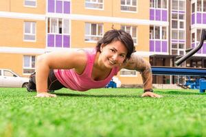 muscular plump woman doing push-up exercises on the sports ground photo