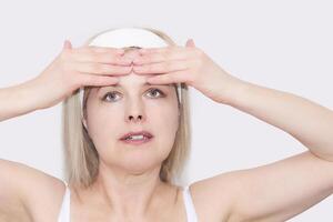 middle-aged woman makes self-massage of the face in the forehead area, close-up portrait photo