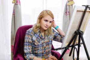 female artist looks at an easel, thinking photo