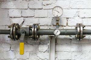 heating pipe with pressure gauge, valve and fittings, against a brick wall photo