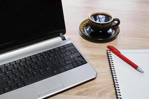 laptop, paper notebook with pen and cup of coffee on the table close-up photo