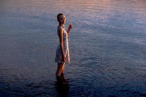 teen girl in a dress by the sea enters the water photo