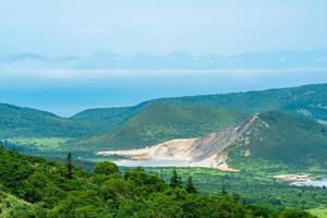 landscape of Kunashir island, geothermal lakes among lava domes in the center of the caldera of Golovnin volcano, Hokkaido island is visible in the distance in the sea photo