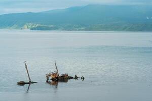 remains of a sunken ship against the backdrop of a sea bay with foggy mountains in the background photo