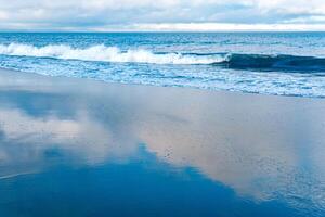 ocean beach with a wave coming back, in which the sky is reflected photo