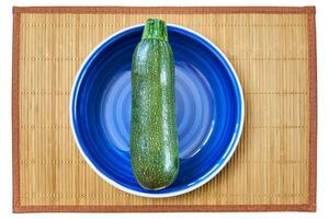 estampado verde calabacín squash en un azul plato en un caña sitio estera foto