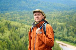 portrait of a man geologist with a backpack and a geological hammer against the wooded mountain landscape photo