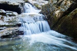 small waterfall in a mountain stream between rocks, the water is blurred in motion photo