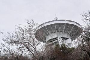 mirror of the astronomical radio telescope, aimed at the sky, is visible from the trees photo
