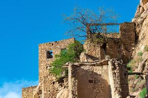 ruins of stone houses attached to the rock in the depopulated village of Gamsutl in Dagestan photo