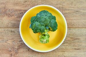 green broccoli inflorescence on a yellow plate on a wooden tabletop photo