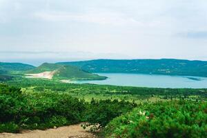 natural landscape of Kunashir island, view of the Golovnin volcano caldera with hot lakes and a path through the thickets of sasa and dwarf pines on a foreground photo