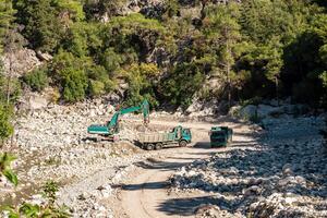 road works in the river valley, excavator and dump trucks move stones photo