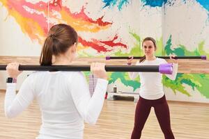 young woman in the gym performs an exercise with a body bar, reflecting in the mirror photo