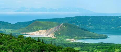 landscape of Kunashir Island, lakes and lava domes in the center of Golovnin volcano caldera, the island of Hokkaido is visible in the distance in the sea photo