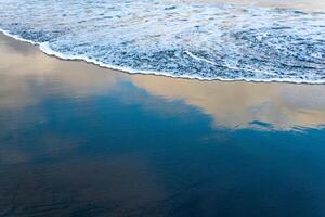 ocean beach with black volcanic sand, the sky is reflected in the rolled back wave of the surf photo