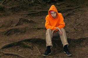 sad teenager in a hoodie sits on a natural background photo