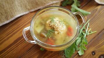 fresh hot soup with chicken meatballs and vegetables in a plate on a wooden table video