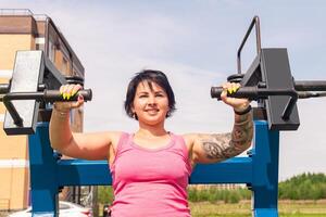 young woman performing exercise using street chest press weight machine in the city yard photo
