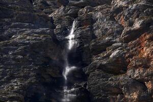 sheer rock wall with a small waterfall flowing down it photo