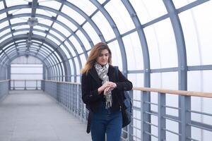 young woman walks along a covered walkway and looks at her watch photo