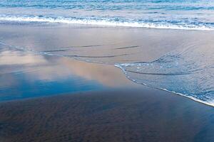 ocean beach with black volcanic sand, the sky is reflected in the rolled back wave of the surf photo