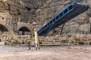 archaeological site among ancient ruins with a conveyor for ground and a theodolite in the foreground photo