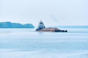 pusher tug pushes dry bulk cargo barge with sand on the river in the morning haze photo