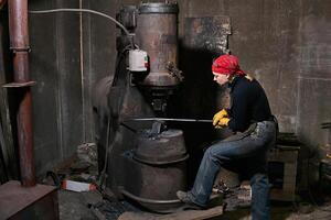 woman blacksmith processes a hot workpiece with a power hammer photo