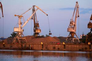 level-luffing bulk-handling cranes load sand onto a barge in a river port in the evening light photo