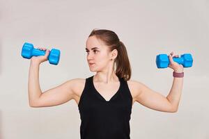 young woman performs an exercise with dumbbells looking to the side, half-length portrait on a light background photo
